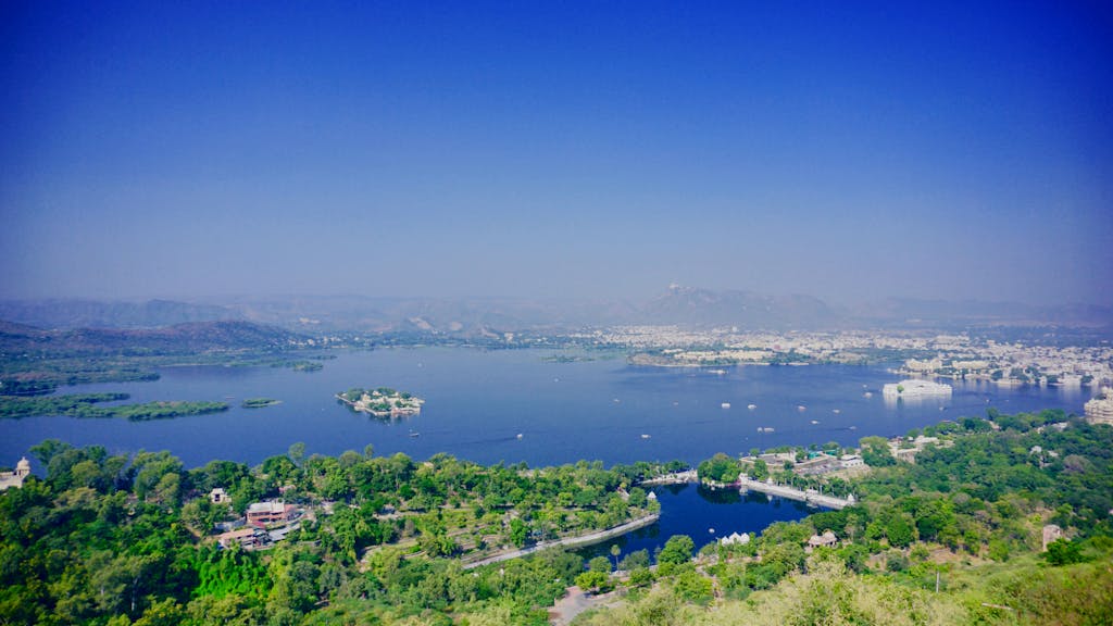 A breathtaking aerial view of Lake Pichola surrounded by lush greenery and Udaipur's cityscape.